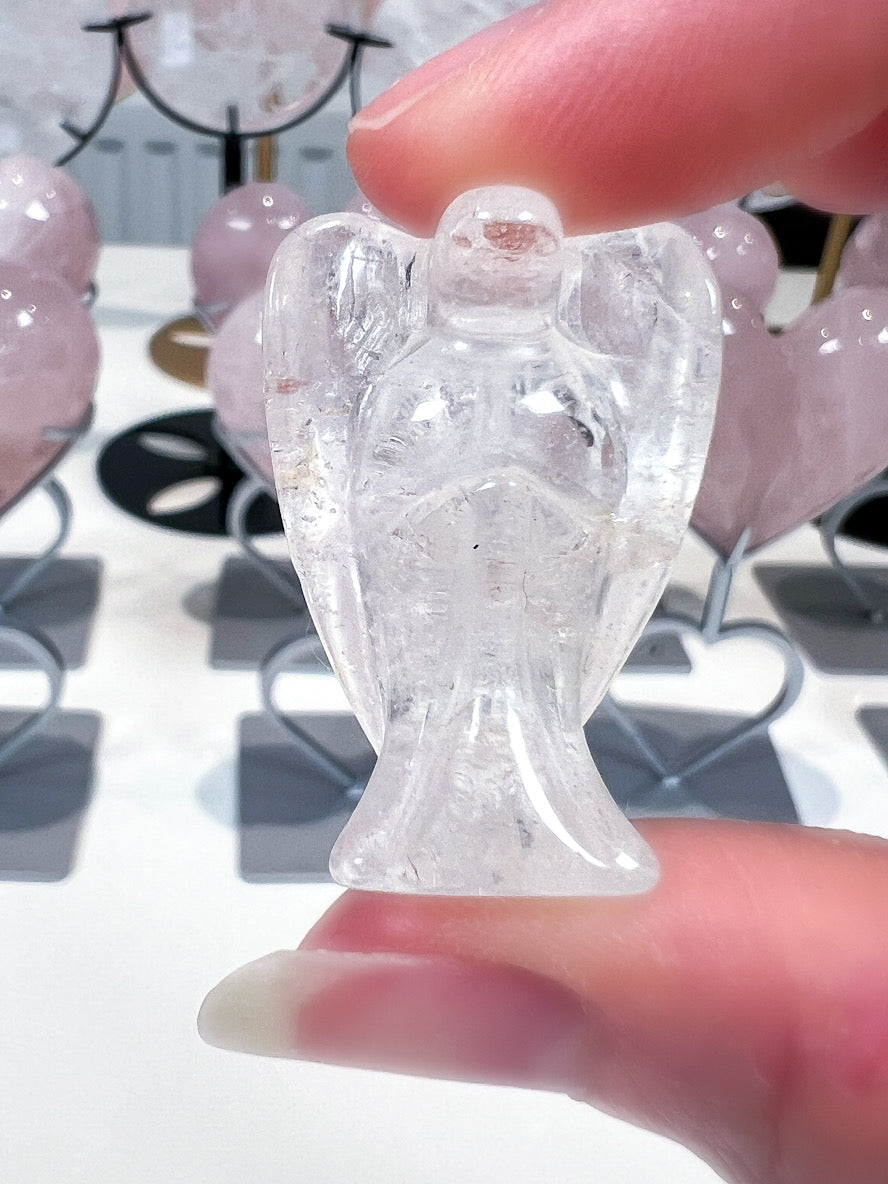 Clear angel figurine held between fingers with a blurred background