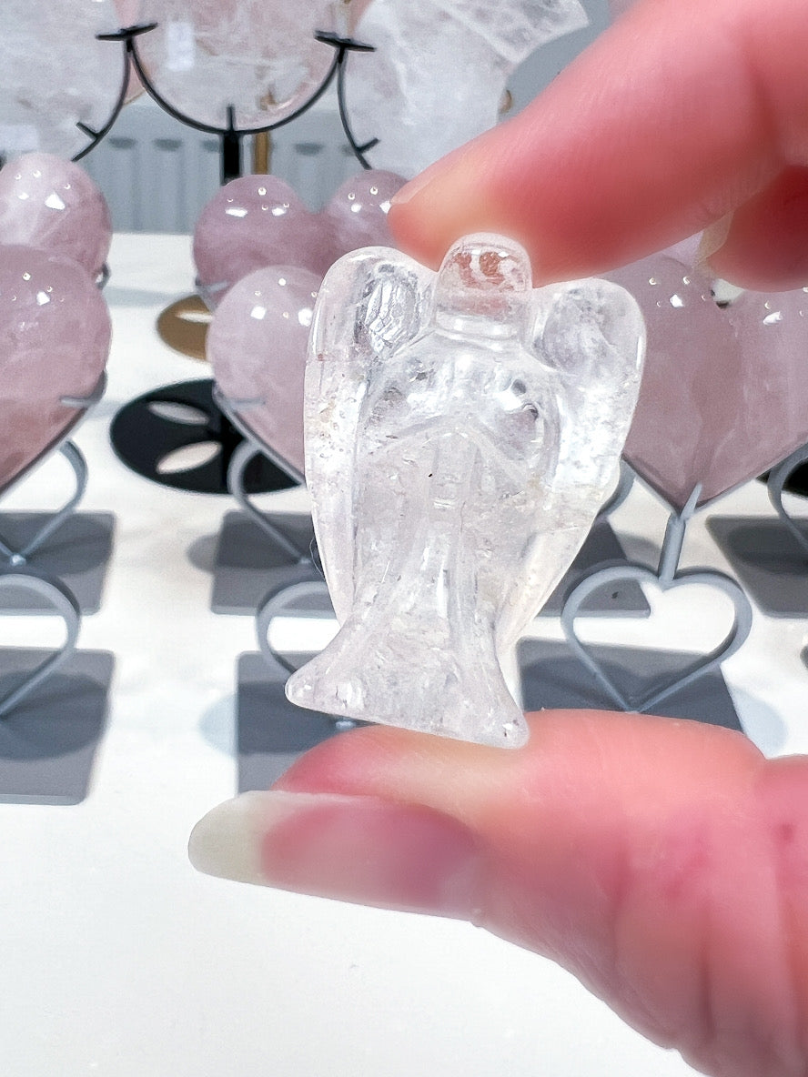 Clear angel figurine held by a hand with a blurred background of similar figurines.
