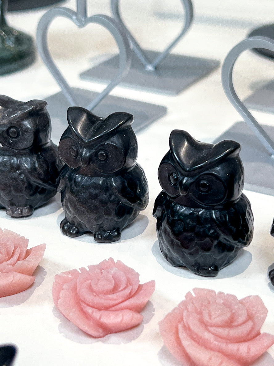 Black owl-shaped crystals and pink rose-shaped crystals on a white surface.
