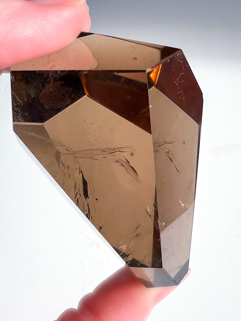 Faceted brown crystal held between fingers against a neutral background