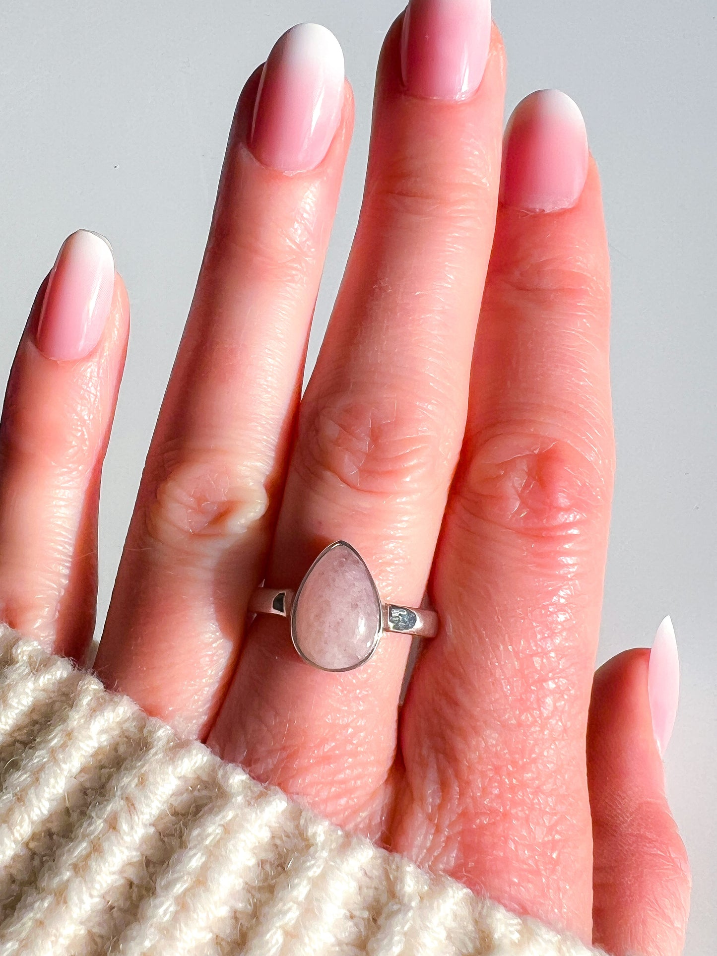 Hand wearing a ring with a pink stone against a neutral background
