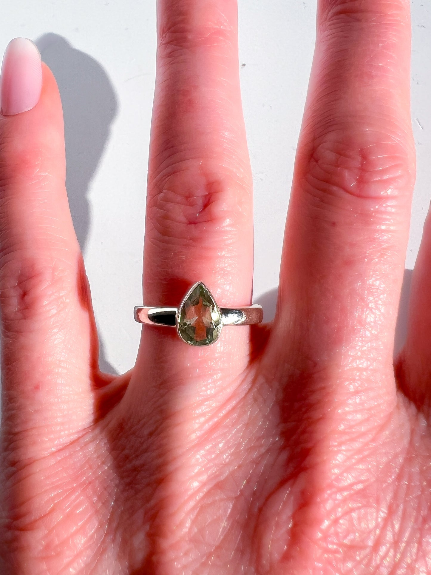 Hand wearing a ring with a green gemstone on a white background
