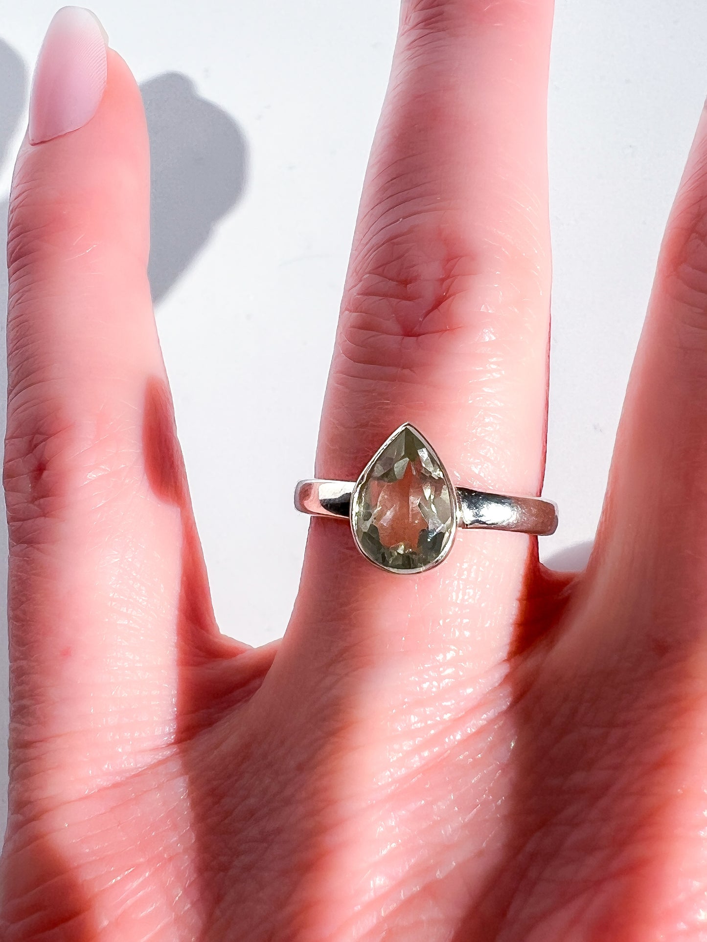 Silver ring with a teardrop-shaped green gemstone on a hand against a white background