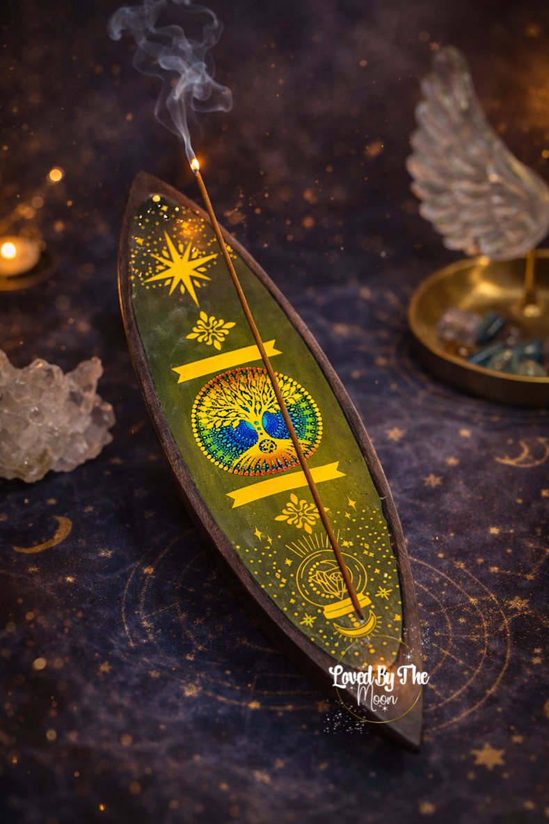 Wooden incense Stick holder with a green and yellow tree of life symbol on it and an incense stick poking out. 