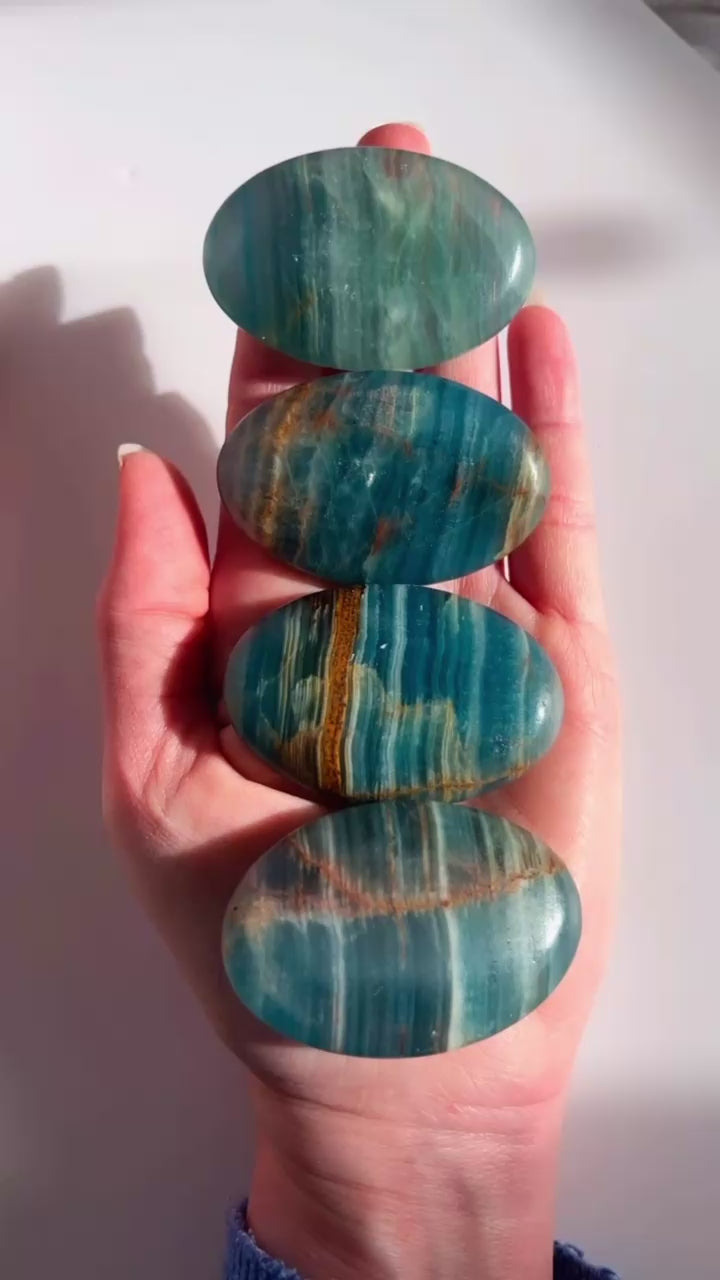 Blue Onyx Palm stones in a hand with a white background