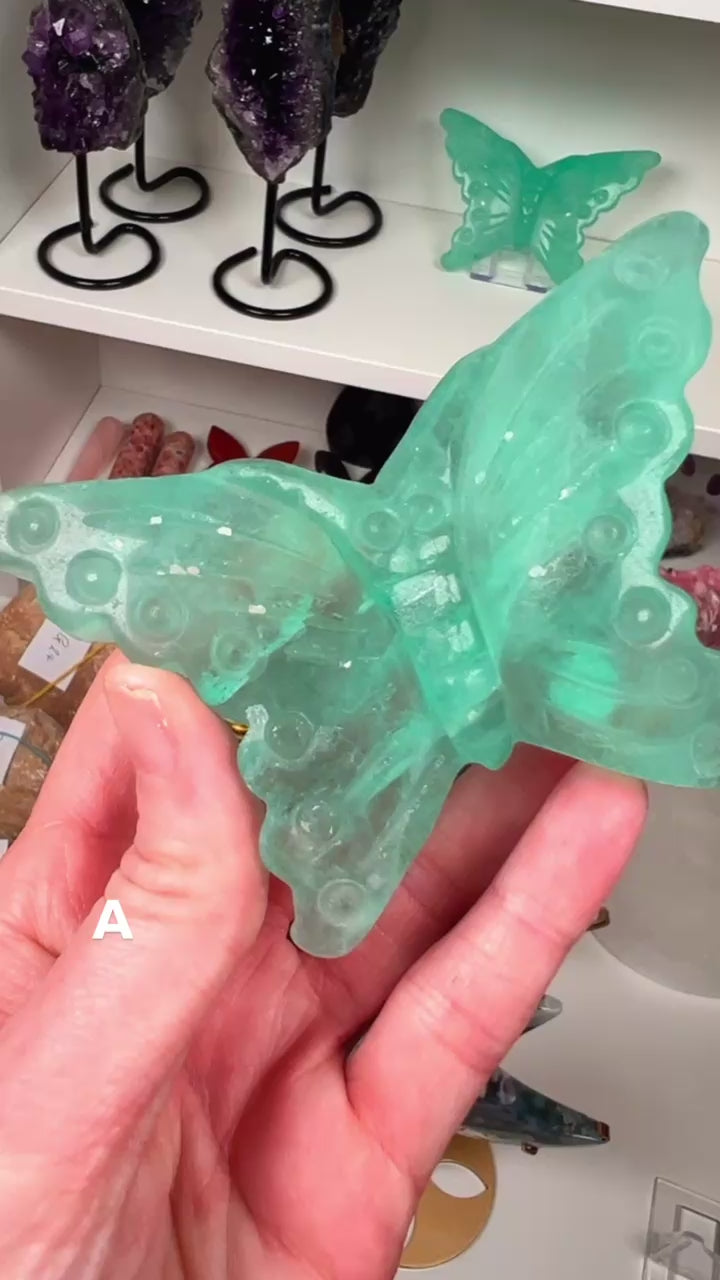 Green Fluorite butterfly in a hand with crystals in the background