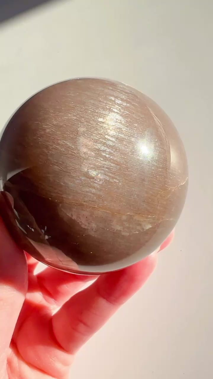 Sunstone Moonstone Sphere in hand with white background.